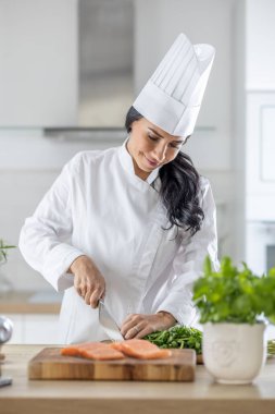 Kadın aşçı olarak çalışıyor. Mutfakta çiğ balık keserken gülümsüyor. İşinden zevk alıyor..