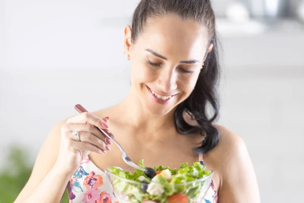 一个面带微笑的黑发姑娘在厨房里尝着健康的沙拉 — 图库照片