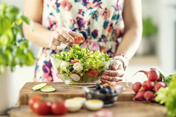 stock image A woman prepares a healthy salad and puts a sliced tomato in a bowl.