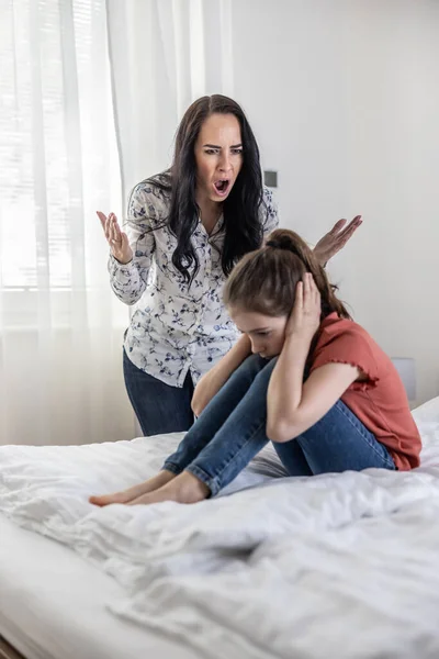 女性はベッドの上に座って彼女の耳をカバー若い女の子で叫ぶように家庭内非物理的な暴力 — ストック写真
