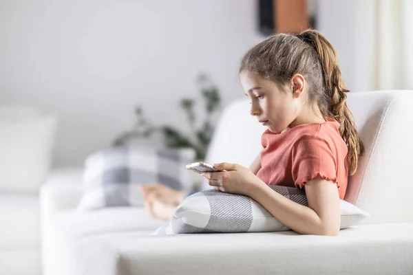 stock image Young preteen girl looks into her phone while having comfortable time at home.