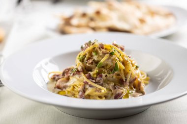 Kızarmış domuz pastırmasından yapılmış spagetti carbonara, yumurtadan sarı sos ve yeşil serpiştirilmiş.