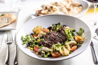 Üzerine biftek dilimleri konulmuş renkli karışık salata..