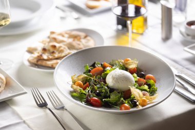 Ortasında Buffalo mozzarella soslu İtalyan salatası. Bir tabak ekmek ve kırmızı şarapla servis ediliyor..