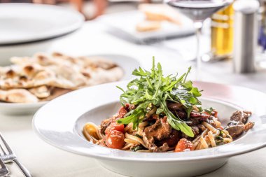 Domatesli makarna ve bir tabakta servis edilen ve roket salatasıyla kaplanmış et..