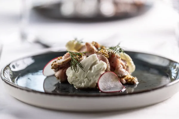 stock image Food styling with pork, cauliflower, mustart seeds, and dressing on a dark plate.