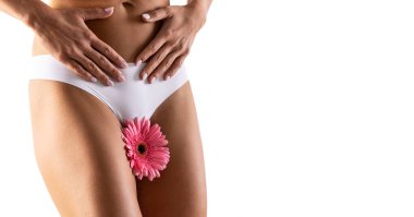 Kasığında pembe bir gerbera olan güzel bir kadın vücudu. Bir kadının rahminde adet döngüsünü ya da hijyeni simgeleyen bir çiçek vardır. Beyazda izole edilmiş.