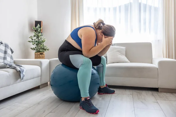 Frustrated obese woman sitting on a swiss ball and crying because of her overweight.