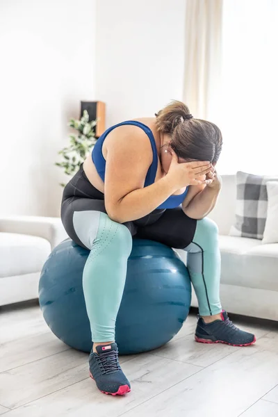 Frustrated obese woman sitting on a swiss ball and crying because of her overweight.