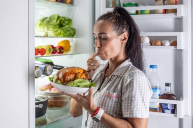 Genç bir esmer, gecenin geç saatlerinde açık buzdolabının önünde kızarmış tavuk yemek için can atıyor..