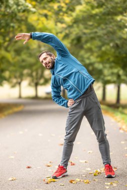 Genç bir atlet parkta koşmadan önce ısınıyor. Vücudun üst kısmını ısıtır..