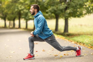 Genç bir atlet parkta koşmadan önce ısınıyor. Vücudun alt kısmını ısıtır..