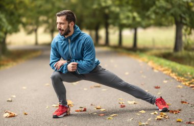 Genç bir atlet parkta koşmadan önce ısınıyor. Vücudun alt kısmını ısıtır..