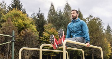 Genç bir sporcu parmaklıklarda antrenman yapar, bacaklarını parmaklıklara paralel kaldırır, midesini ve bacaklarını güçlendirir..