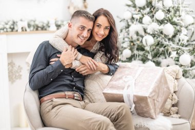 Bir Noel ağacı ve kutsanmış bir Noel hediyesinin yanında oturan kadın ve erkek sarılır..