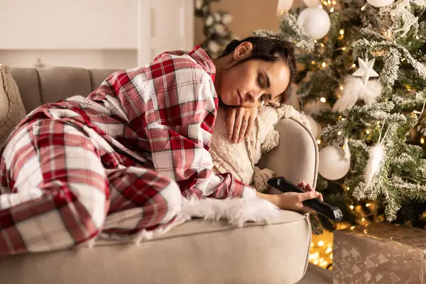 パジャマの若い女性は クリスマス放送を見ながらテレビの前でソファーで眠った ロイヤリティフリーのストック画像