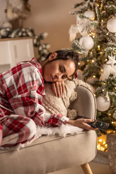 パジャマの若い女性は クリスマス放送を見ながらテレビの前でソファーで眠った ストック写真