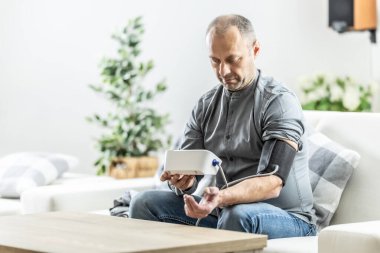 Olgun bir adam evdeki kan basıncını dijital tansiyon monitörüyle ölçüyor..