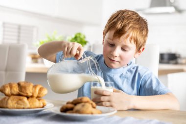 Küçük bir çocuk kahvaltıda kendine taze süt dolduruyor..