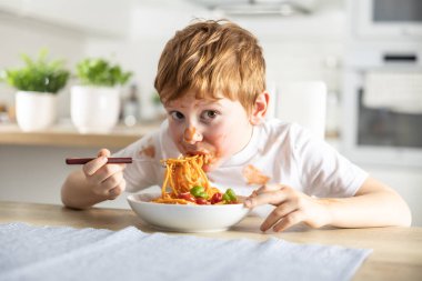 Küçük tatlı bir çocuk evde öğle yemeği için spagetti bolonez yiyor ve ketçapla kaplanmış..