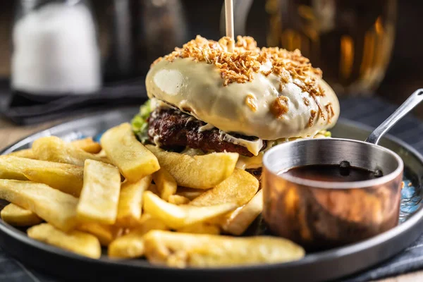 Beef burger topped with cheese with fries and draft beer on a pub or restaurant plate.
