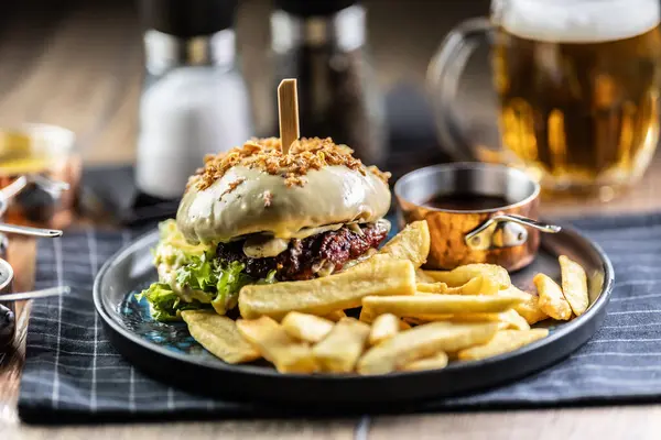 Beef burger topped with cheese with fries and draft beer on a pub or restaurant plate.