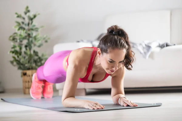 A beautiful fitness woman in sportswear is doing plank exercises. He trains at home in his living room on a mat.