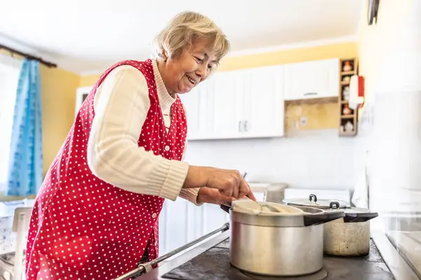 Grandma cooks bryndzove halusky, a traditional Slovak dish, on her old oven. A pensioner cooks food in her kitchen.