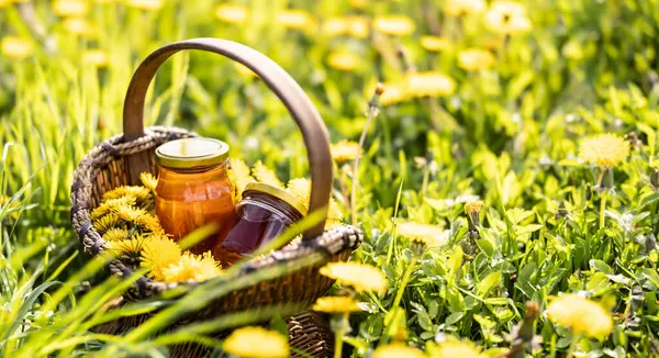 草原のどこかに置かれた蜂蜜の瓶が付いているウィッカーのバスケットのタンポポの花 ストック写真