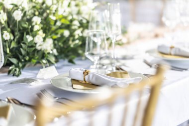 Çiçekler, mumlar, bardaklar ve çatal bıçaklarla süslenmiş beyaz bir masa örtüsüyle kaplı bir düğün masası..