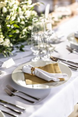 Çiçekler, mumlar, bardaklar ve çatal bıçaklarla süslenmiş beyaz bir masa örtüsüyle kaplı bir düğün masası..