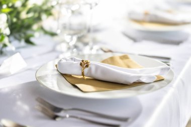 Çiçekler, mumlar, bardaklar ve çatal bıçaklarla süslenmiş beyaz bir masa örtüsüyle kaplı bir düğün masası..