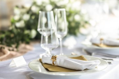 Çiçekler, mumlar, bardaklar ve çatal bıçaklarla süslenmiş beyaz bir masa örtüsüyle kaplı bir düğün masası..