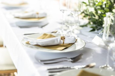 Çiçekler, mumlar, bardaklar ve çatal bıçaklarla süslenmiş beyaz bir masa örtüsüyle kaplı bir düğün masası..