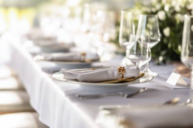 Çiçekler, mumlar, bardaklar ve çatal bıçaklarla süslenmiş beyaz bir masa örtüsüyle kaplı bir düğün masası..