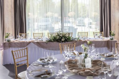 Çiçekler, mumlar, bardaklar ve çatal bıçaklarla süslenmiş beyaz bir masa örtüsüyle kaplı bir düğün masası..