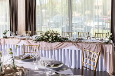 Çiçekler, mumlar, bardaklar ve çatal bıçaklarla süslenmiş beyaz bir masa örtüsüyle kaplı bir düğün masası..