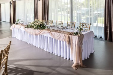 Çiçekler, mumlar, bardaklar ve çatal bıçaklarla süslenmiş beyaz bir masa örtüsüyle kaplı bir düğün masası..