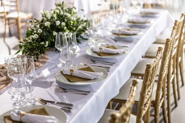 Çiçekler, mumlar, bardaklar ve çatal bıçaklarla süslenmiş beyaz bir masa örtüsüyle kaplı bir düğün masası..