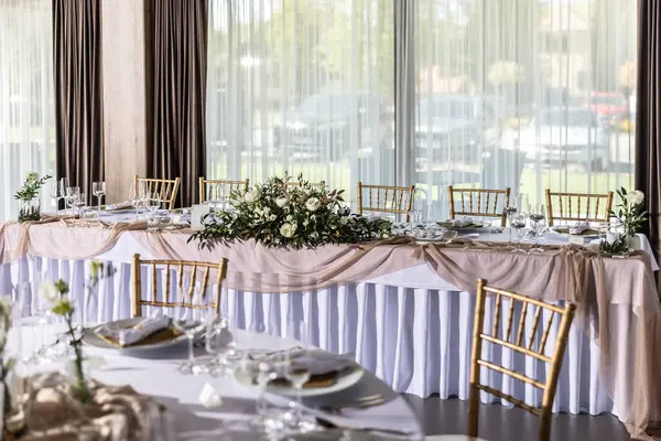 Çiçekler, mumlar, bardaklar ve çatal bıçaklarla süslenmiş beyaz bir masa örtüsüyle kaplı bir düğün masası..