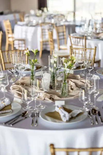 Çiçekler, mumlar, bardaklar ve çatal bıçaklarla süslenmiş beyaz bir masa örtüsüyle kaplı bir düğün masası..