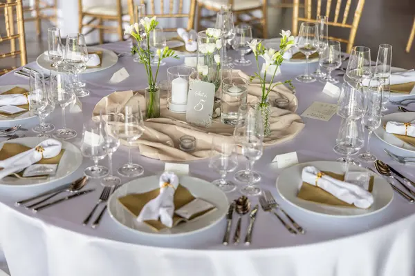 Çiçekler, mumlar, bardaklar ve çatal bıçaklarla süslenmiş beyaz bir masa örtüsüyle kaplı bir düğün masası..