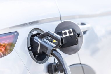 Focus closeup electric vehicle plugged in with EV charger device from blurred background of public charging station powered by renewable clean energy for progressive eco-friendly car concept.