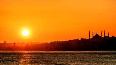 Güneş ufukta, Boğaz 'ın üzerinde batıyor. Mavi Cami 'nin arka planında bir kargo gemisinin silueti. Seçici odak.