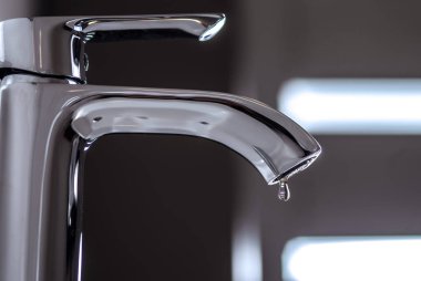 Drops of water from the mixer drip into the sink. Selective focus. clipart