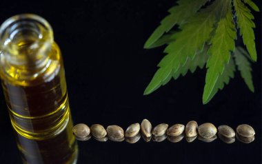 Cam şişede kenevir tohumu ve aynanın siyah arka planında marihuana yaprağı olan kenevir yağı. Seçici odak.