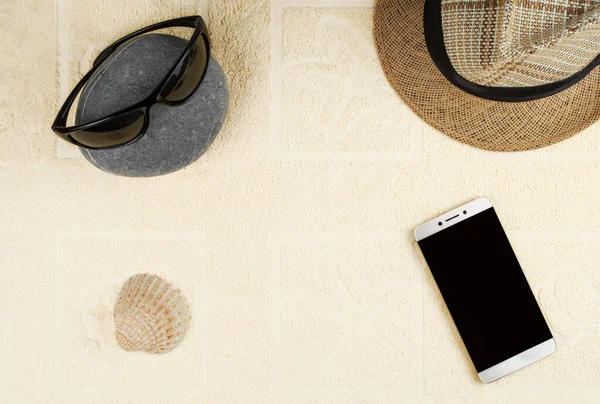 stock image A smartphone with a blank screen, a straw hat, sun glasses, and a shell in the background of a beach towel. 