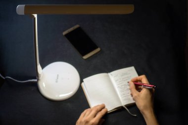 Masa lambası elinde kalem, not defterinde koyu mavi arka plan. Seçici odak.  