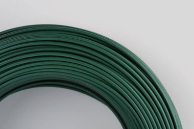 A coil of green PVC coated wire. Isolated on a light grey background. Industrial texture. Selective focus