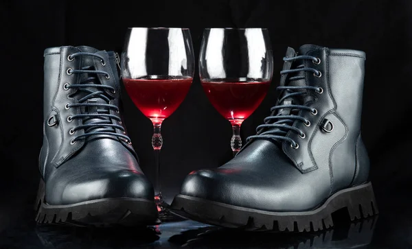 A pair of men\'s boots with two glasses of red wine. On a black background.